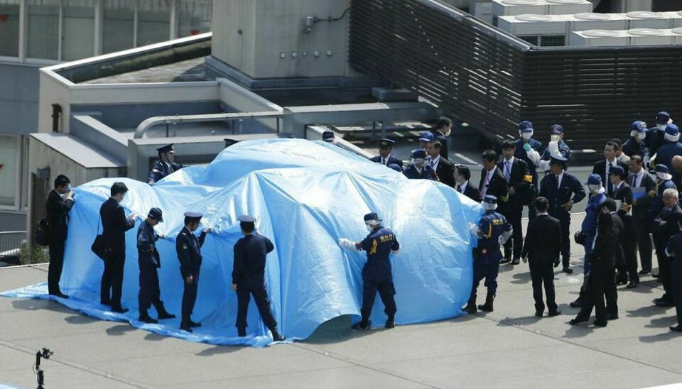 Politi sikkerhedspersonale dækker med en presenning for en drone, der landede på den japanske premierministers tag. Foto: TORU HANAI/Scanpix