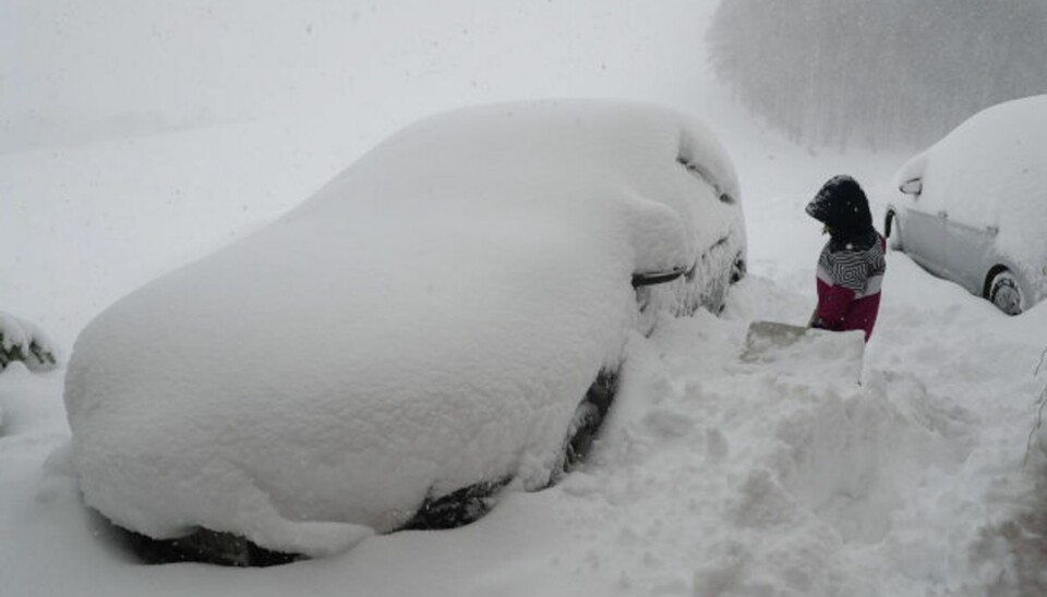 En dreng forsøger at fjerne sne fra en bilrude i den østrigske by Salzburg lørdag 5. januar. Foto: Franz Neumayr/AFP