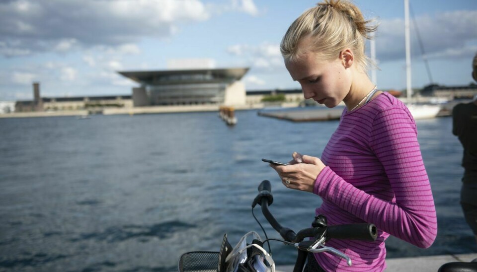 Ung kvinde med cykel ved Københavns Havn - med udsigt til Operaen - skriver på sin smartphone.