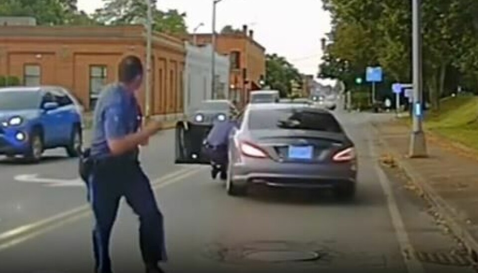 Betjenten hænger halvt ude af bilen og falder til sidst ned på gaden.