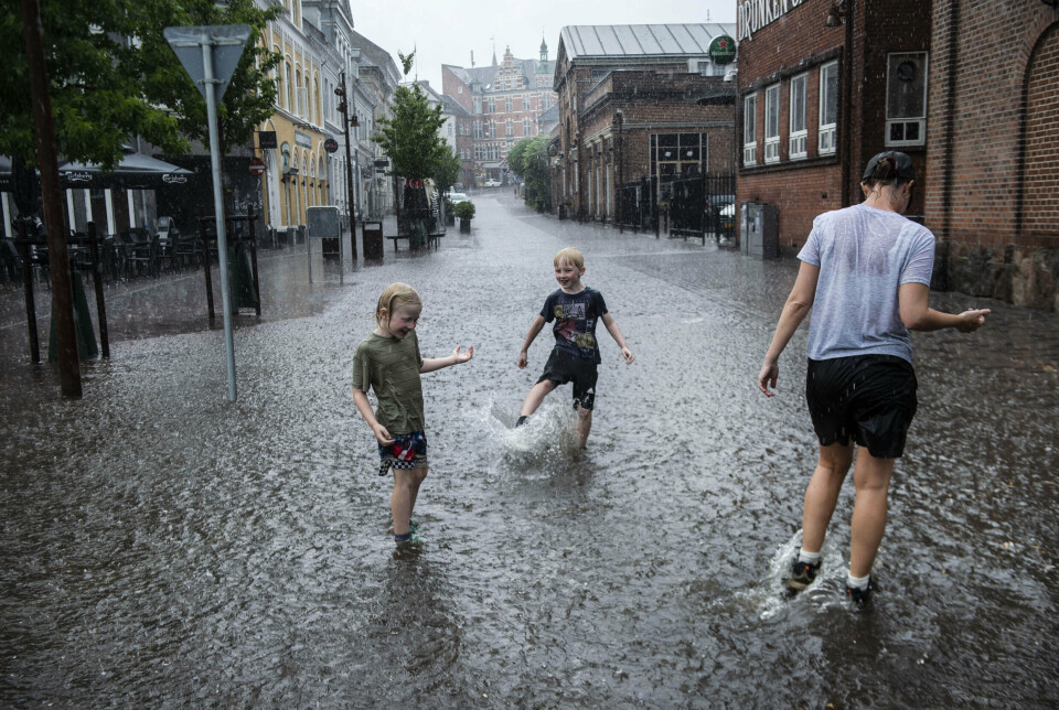 Drenge i regnen på den oversvømmede Frederiksgade i Svendborg på Fyn, mandag den 26. juni 2023. Denne weekend byder på risiko for kraftige byger, hvor der falder mere end 15 millimeter på 30 minutter. (Arkivfoto).