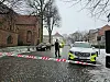 Politiafspærret brostensgade med patruljevogn, ambulance og kirke i snevejr
