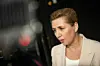 Statsminister Mette Frederiksen i lys blazer ses i profil under interview i et mørkt studie.
