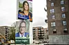 Valgplakater på lygtepæl foran moderne lejlighedsbygninger i byen