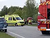 Redningsfolk ved en trafikulykke på en landevej med ambulance og stort rødt køretøj.