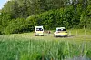 To redningskøretøjer står på et græsareal foran en tæt grøn skovkant.