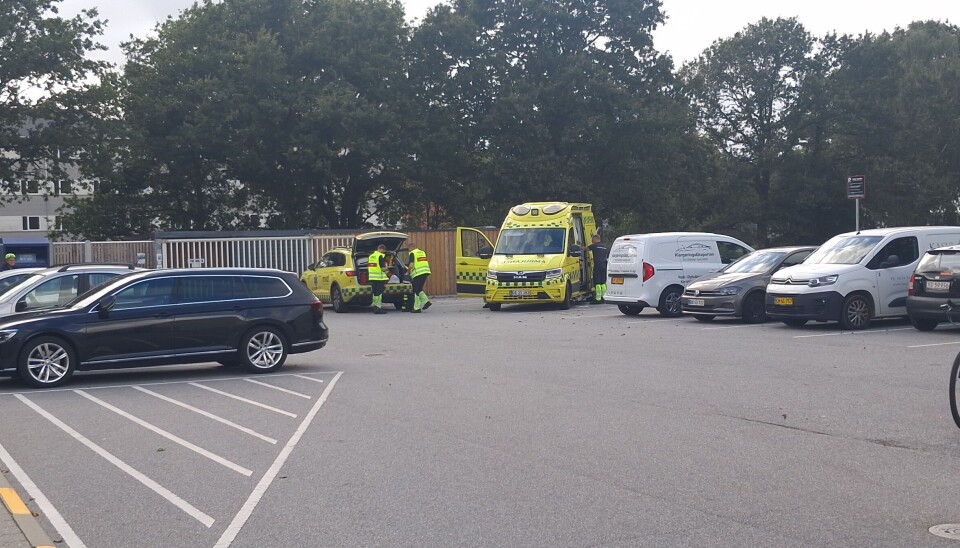 Udrykningskøretøjer og redningspersonale på en parkeringsplads med biler og en cykel.