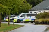 To politibiler parkeret ved en bygning i grønne omgivelser.