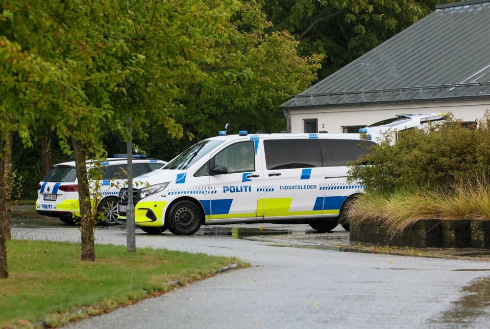To politibiler parkeret ved en bygning i grønne omgivelser.