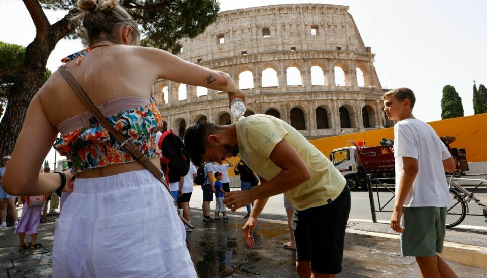 En kvinde hælder tirsdag under en hedebølge vand på nakken af en mand foran Colosseum i Rom.
