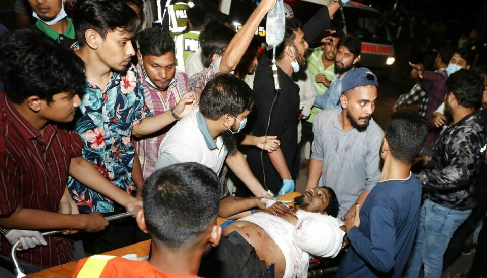Redningsarbejdere og civile bærer en af de tilskadekomne væk efter en brand på et stort containerdepot i Bangladesh.