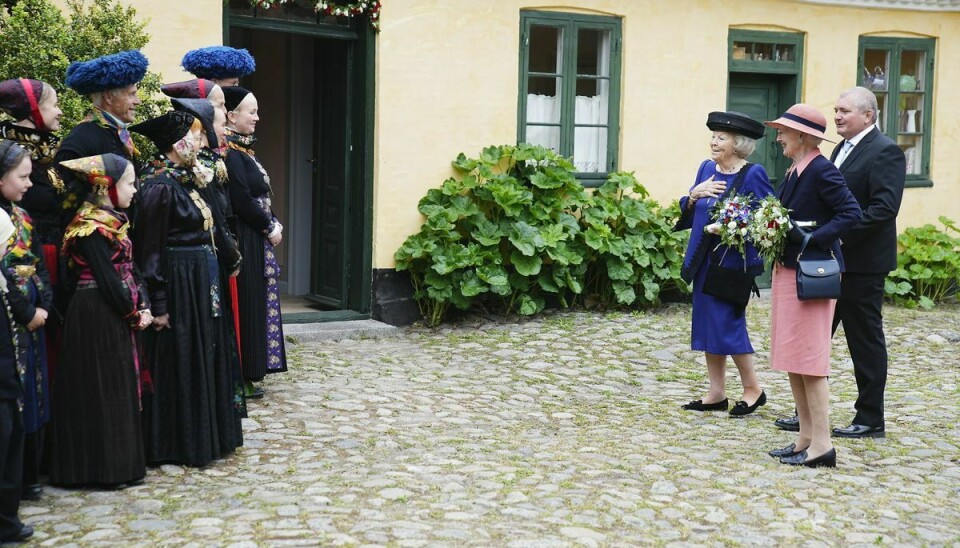 Dronningen og en tydeligt benovet prinsesse Beatrix betragter en gruppe mennesker i farvestrålende folkedragter.