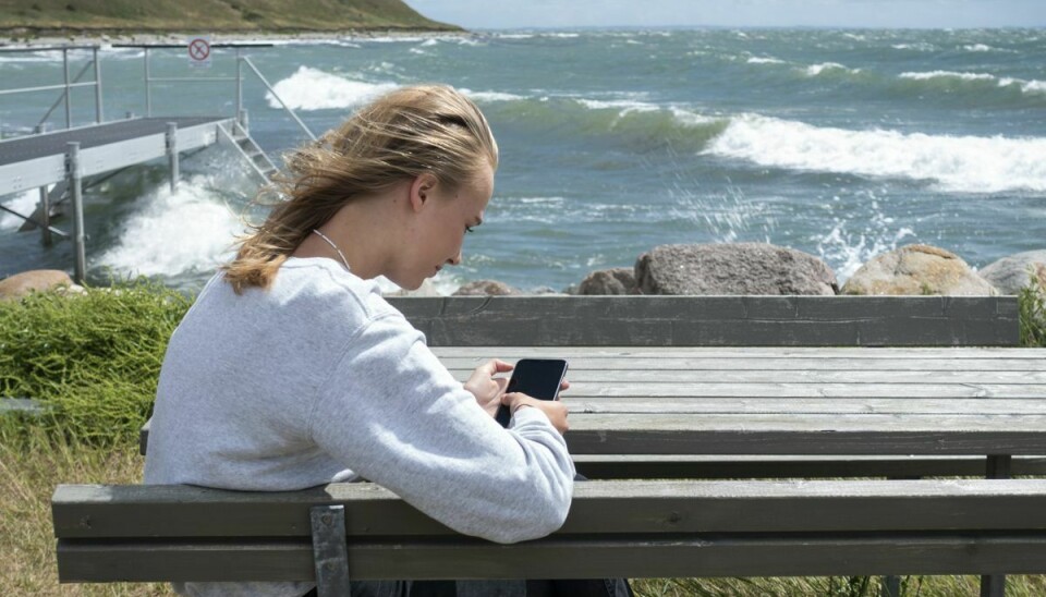 Teenagepige med mobil smartphone ved badebro i Sejerø Havn. Sejerø er en 12 kilometer lang ø i Sejerøbugten i Kattegat cirka 5 kilometer vest for Sjælland. (Arkivfoto)