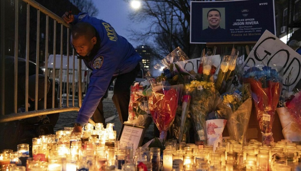 En betjent fra politistyrken i New York City tænder et lys for den 22-årige kollega, der fredag blev dræbt af skud i en lejlighed i bydelen Harlem. Mandag er den mand, som politiet har identificeret som drabspersonen, død.