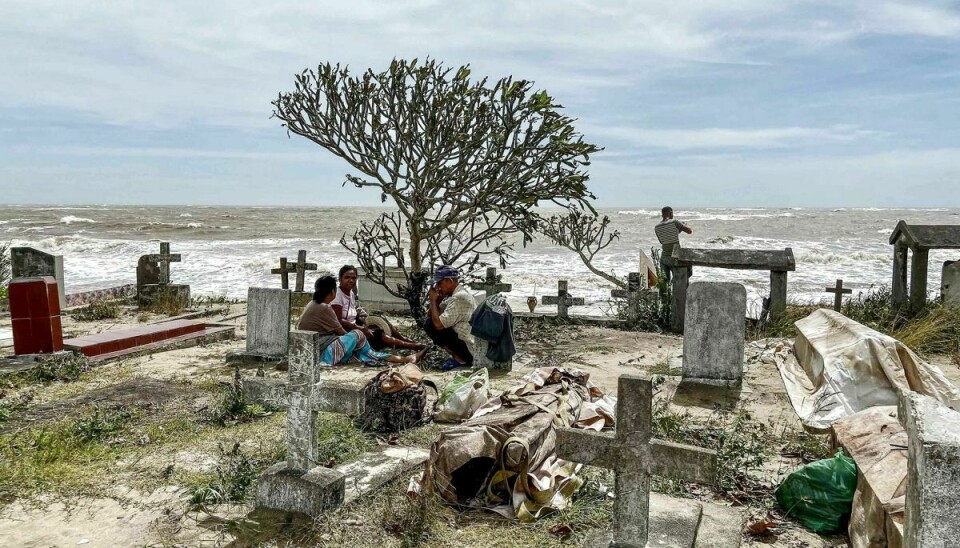 Pårørende sidder ved siden af nogle af de lig, der blev skyllet ud af deres grave på den lokale kirkegård i byen Mahanoro. Kirkegården ligger ud til havet, og de kraftige bølger fjernede meget af den sandede jord, de afdøde var begravet under.