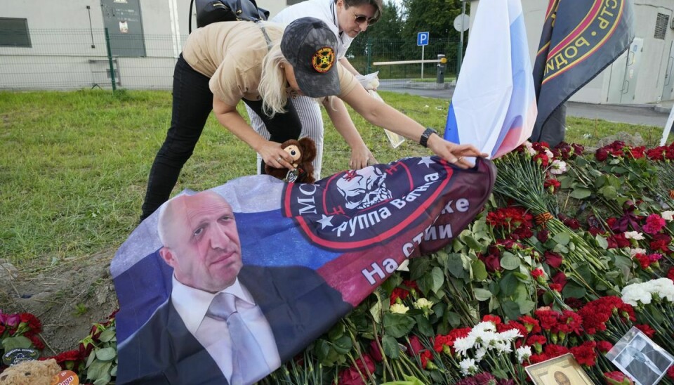 Der er fredag lagt blomster frem, mens en kvinde placerer et billede af Jevgenij Prigozjin ved Wagner-gruppens hovedkvarter i Sankt Petersborg.
