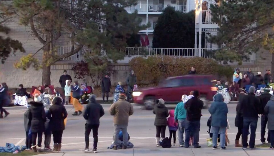 Den røde suv, som blev styret ind i en menneskemængde under en juleparade i byen Waukesha i Wisconsin, ses gasse op i baggrunden. Billedet er taget, kort før bilen ramte deltagere i paraden.