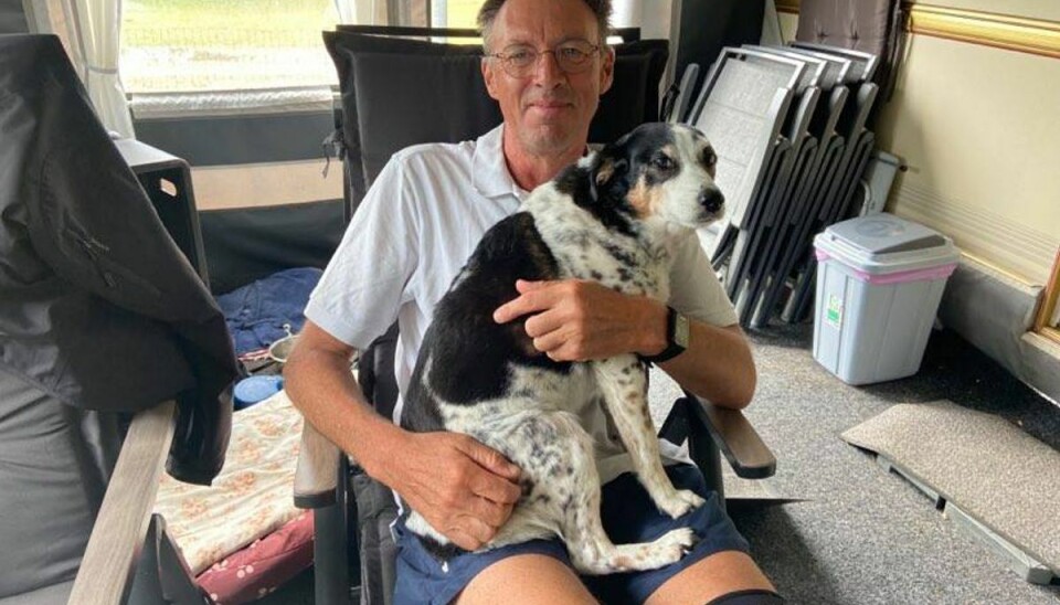 57-årige John Bjørn hygger sig med hunden Tilde i campingvognens fortelt på trods af det triste vejr. Campisten ser bare noget fjernsyn, hvis ikke vejret er til en cykeltur.