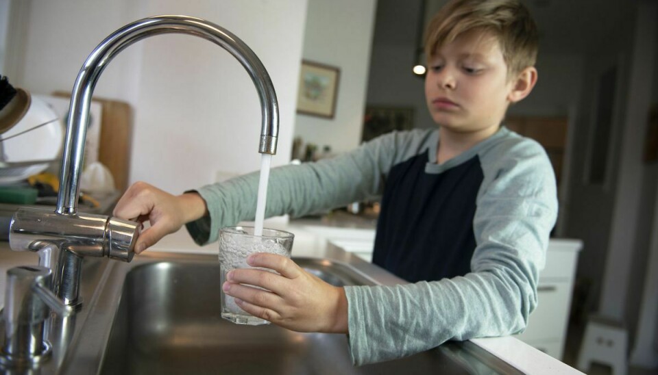 Dreng tager vand i vandglas fra vandhane ved køkkenvask i køkken i lejlighed.